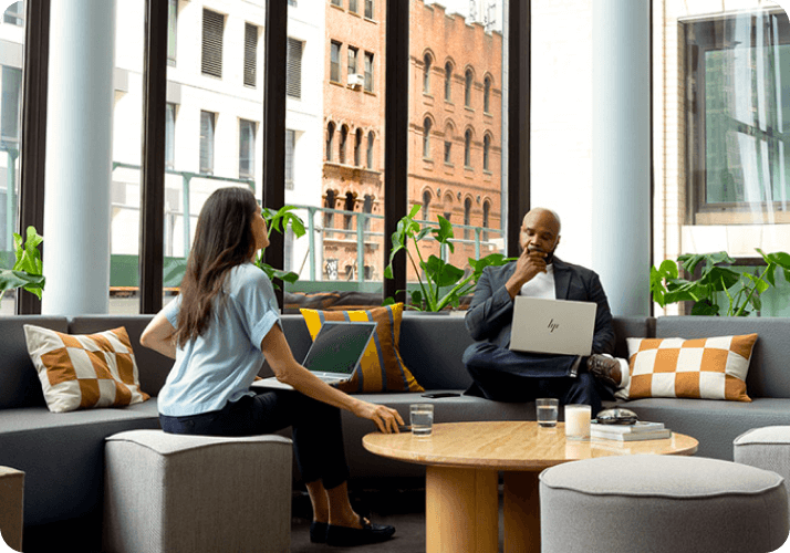 Un hombre y una mujer con laptops HP en una oficina participando en una reunión y compartiendo ideas