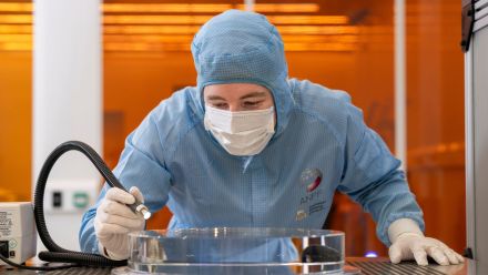 Technical officers manoeuvre glass substrate prior to polishing in the ANU Research School of Physics cleanroom.